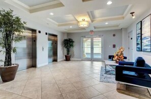 A hotel lobby with a reception desk, seating area, potted plants, and an elevator.