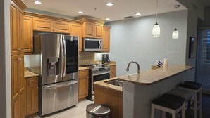 A modern kitchen with wooden cabinets, stainless steel appliances, granite countertops, and pendant lighting.
