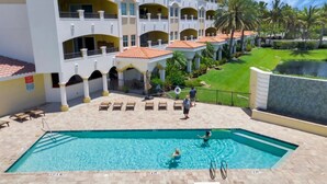 A swimming pool area with lounge chairs, a pool deck, and a building with balconies and a tiled roof.