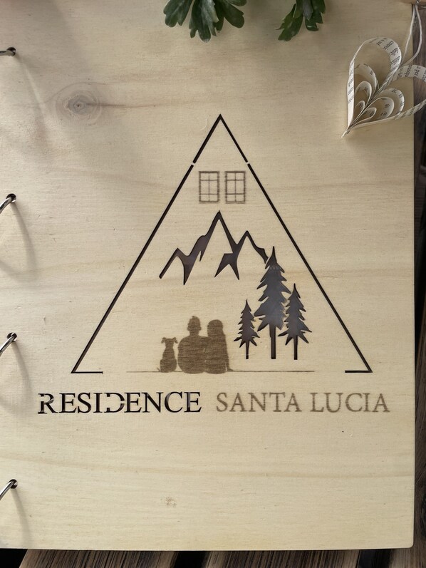 Ein hölzernes Schild mit einer Berg- und Baumsilhouette, sowie dem Text "RESIDENCE SANTA LUCIA".