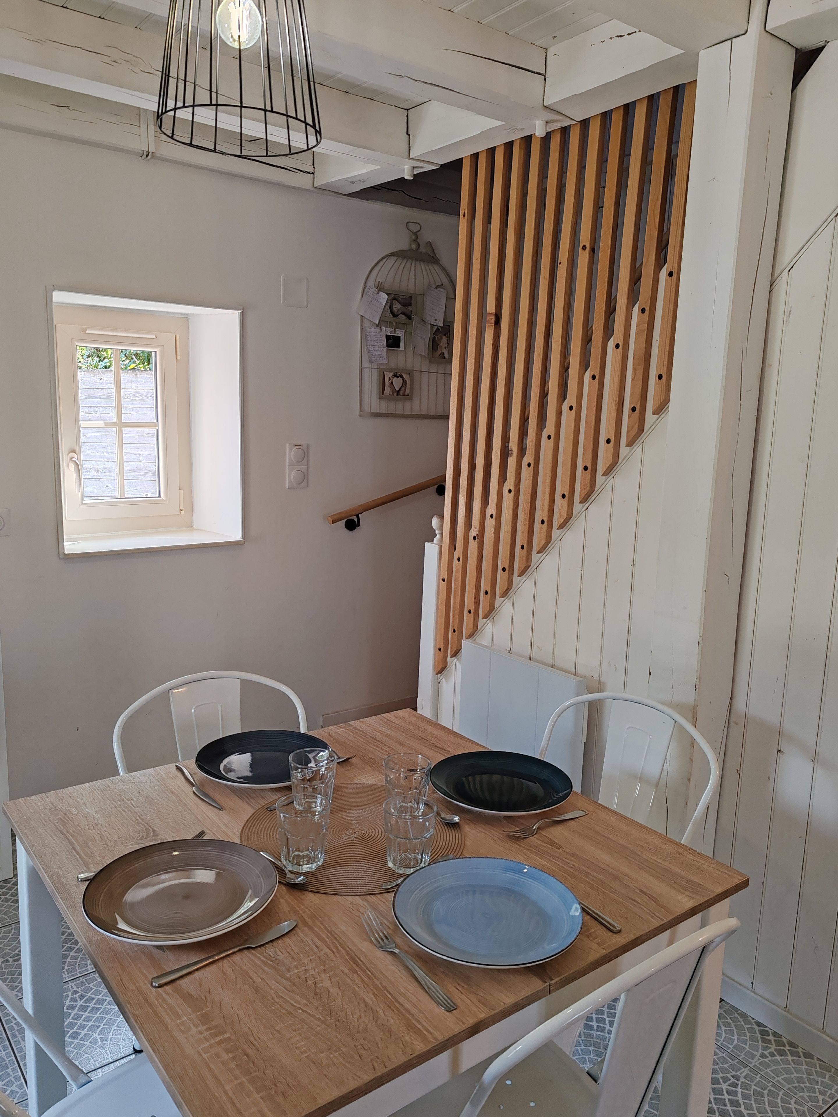 A dining area with a wooden table set for two, two chairs, and a window with a view.