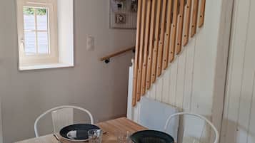 A dining area with a wooden table set for two, two chairs, and a window with a view.