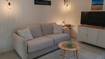 Un salon comprenant un canapé, une table basse, un téléviseur et des luminaires fixés au mur.
