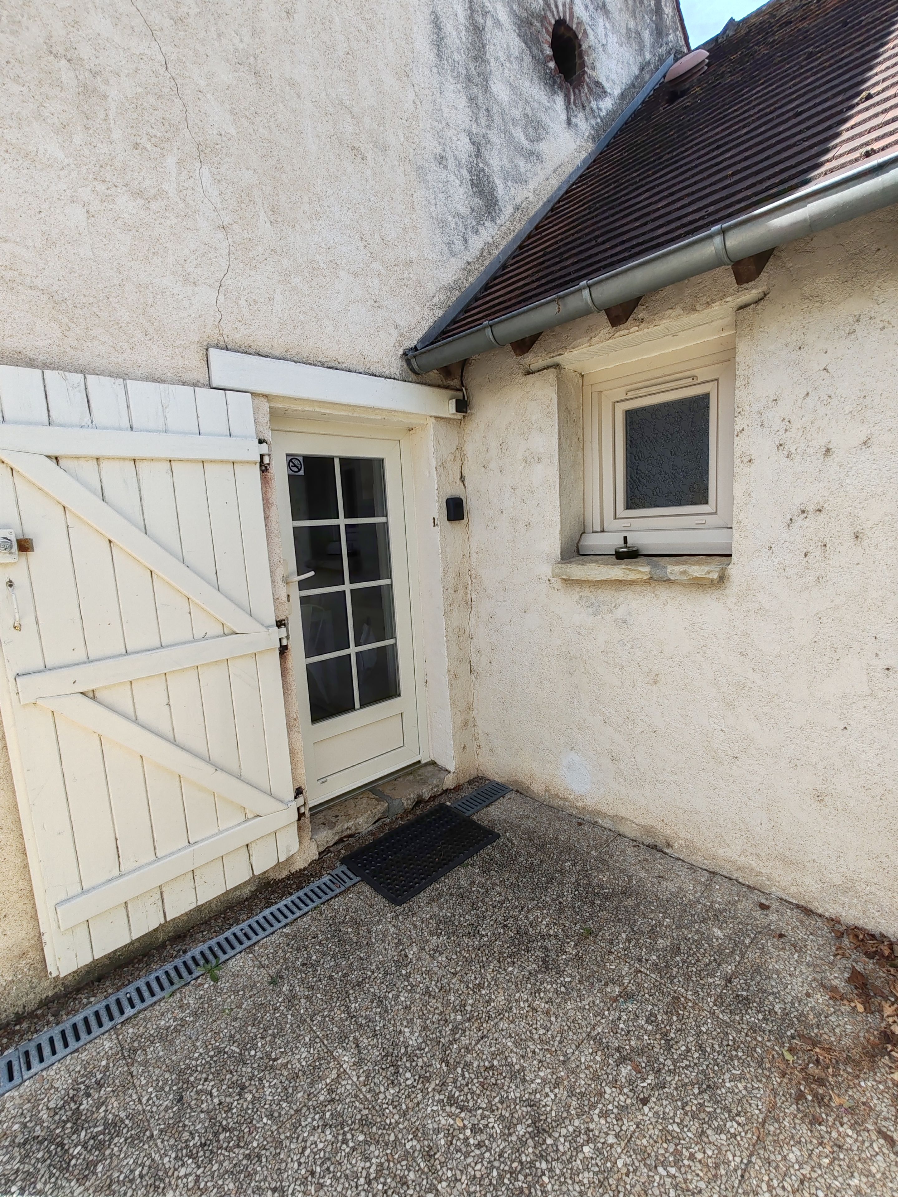 Un bâtiment à l’extérieur blanc, doté d’une entrée fermée par un portail, d’une fenêtre et d’un petit porche.