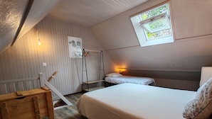 Una habitación acogedora con suelo de madera, una litera con colchón blanco, un banco de madera, una mesita pequeña, una lámpara de pared y una ventana con vistas a árboles.