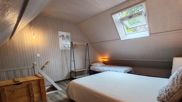 A cozy room with a wooden floor, a bunk bed with a white mattress, a wooden bench, a small table, a wall-mounted light, and a window with a view of trees. - Cottage in Sully sur Loire (Sully-sur-Loire)