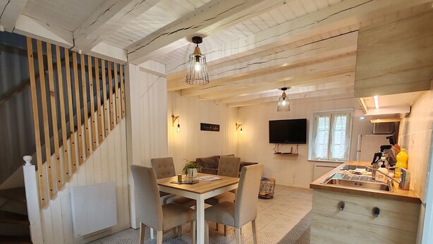 Un comedor acogedor y bien iluminado con una mesa y sillas de madera, una escalera con barandilla y una cocina con lavaplatos y encimera.