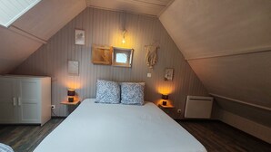 Une chambre à coucher avec un grand lit, deux lampes de chevet, une armoire en bois, une petite fenêtre et un luminaire fixé au mur.
