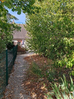 Camí de grava que condueix a una casa amb teulada de maó, envoltada de vegetació densa i una tanca verda.