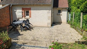 Un patio con una mesa, sillas, un ventanal pequeño y un camino de grava.