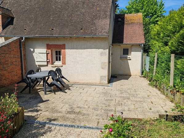 A patio with a table and chairs, a small window, and a gravel path. - Cottage in Sully sur Loire (Sully-sur-Loire)