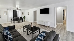 A spacious living room with a black coffee table, grey sofas, and a flat-screen TV mounted on the wall. - Serene 3BR Luxe Easy Access to NRG & Galleria (Houston)