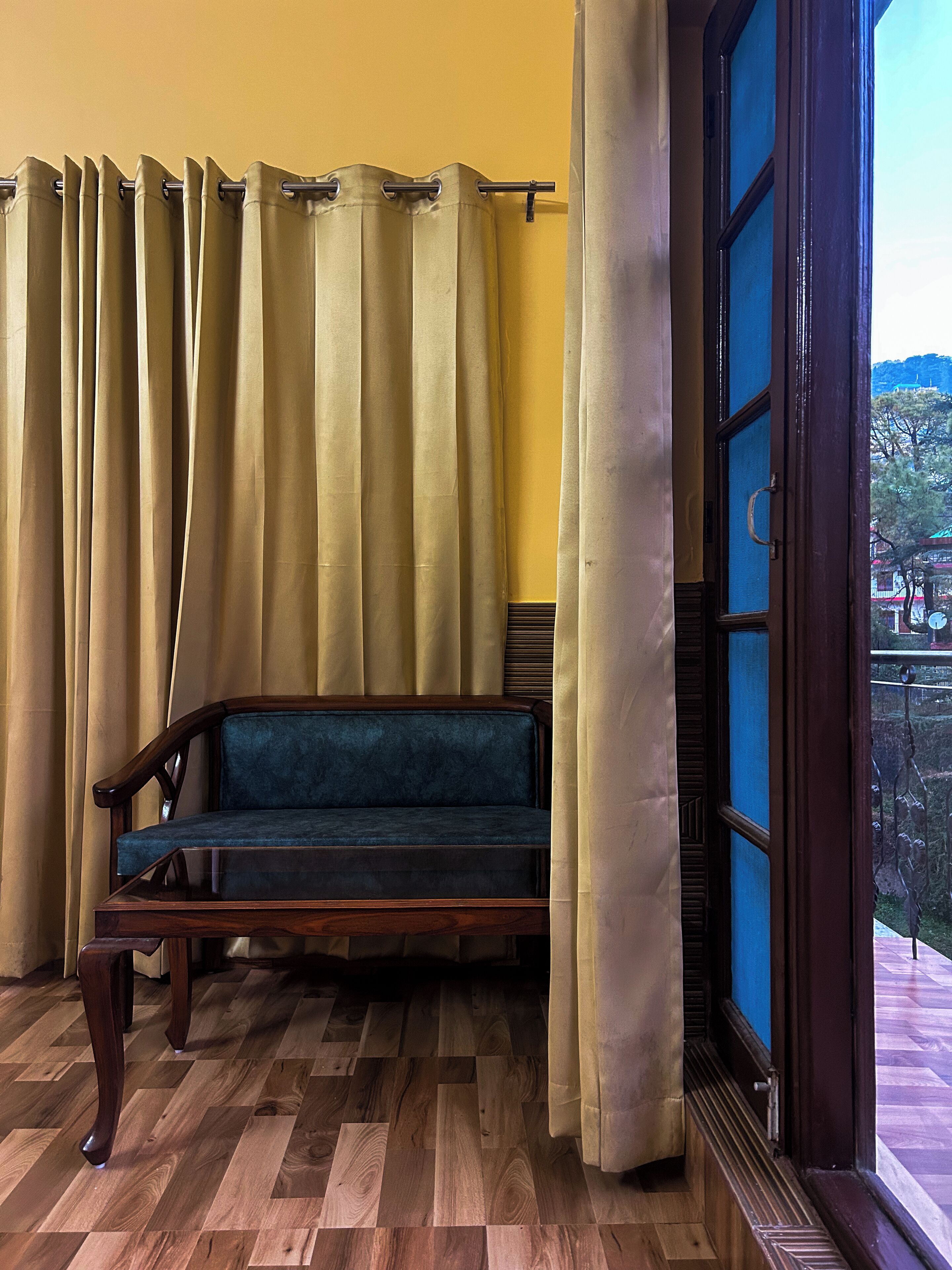 A room with a wooden bench, yellow walls, and a window with a view of a building.