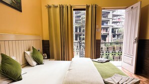 Una camera d'albergo con un letto, cuscini verdi, una finestra con tende e vista sugli edifici.