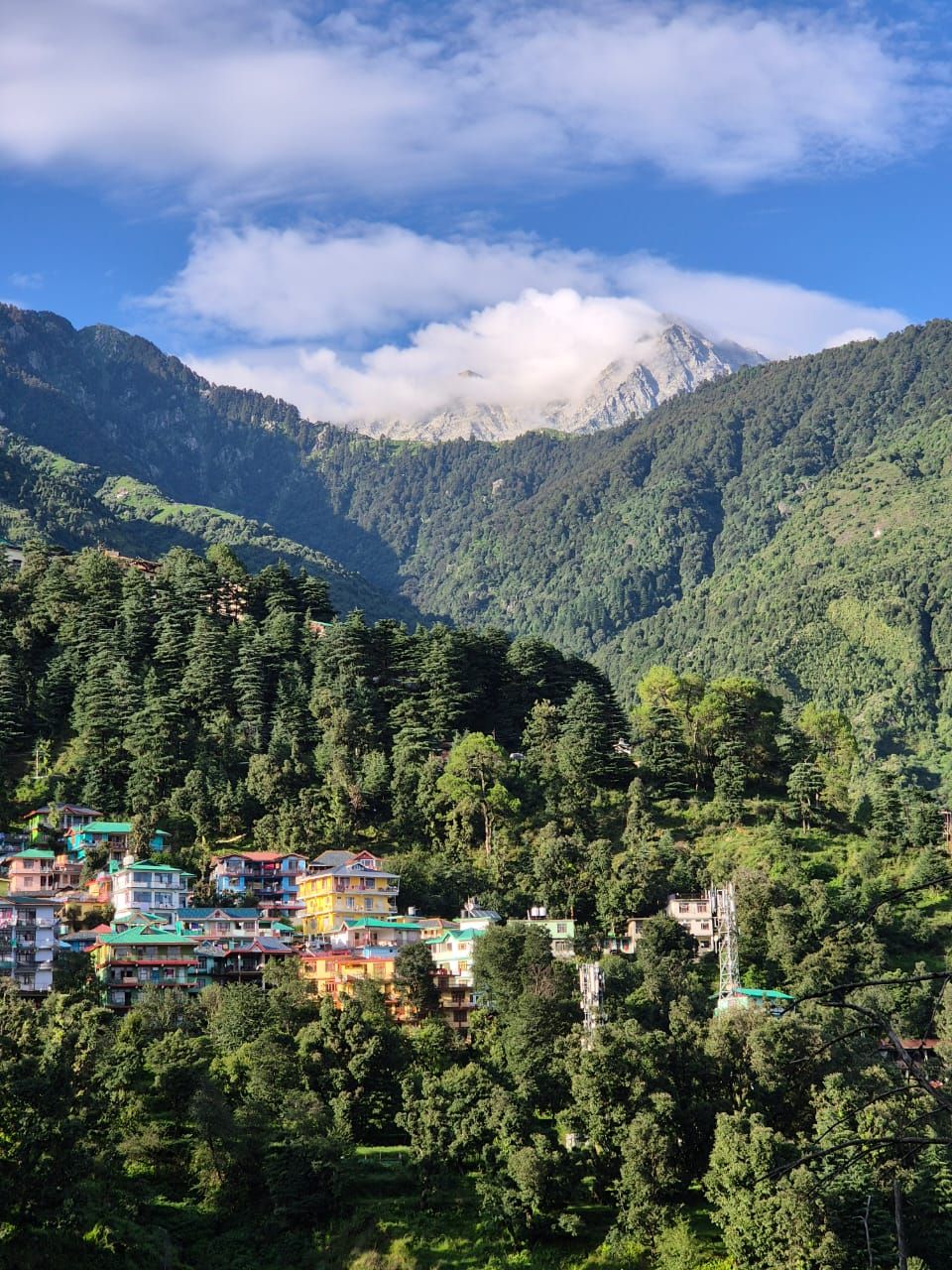 Un paysage montagneux où l’on aperçoit un ensemble de bâtiments aux couleurs vives, nichés au milieu de forêts denses.