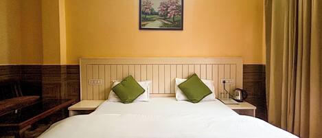 A hotel room with a bed, green pillows, a nightstand, a painting, and a window with curtains.