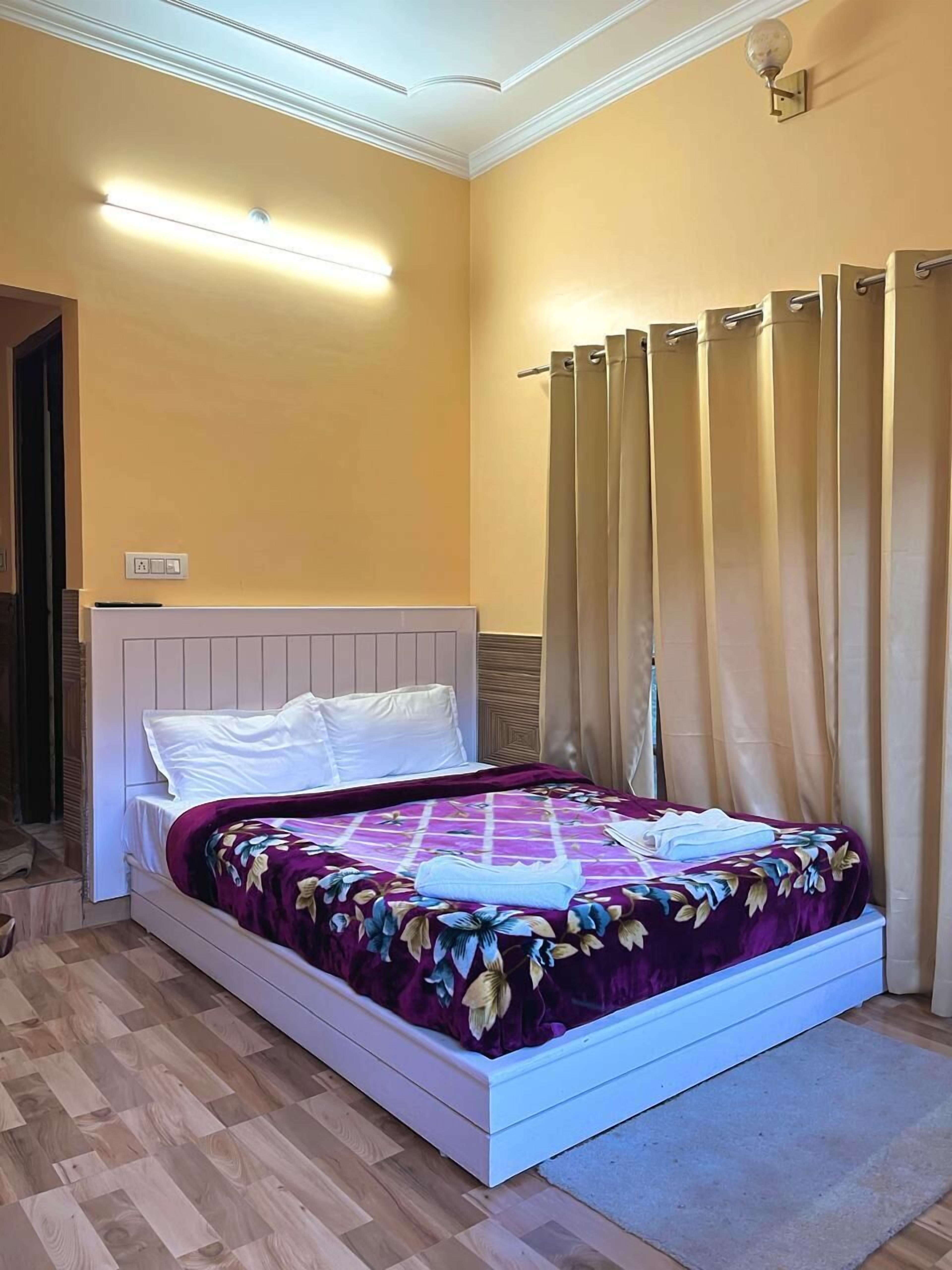 A bedroom with a bed, wooden flooring, a headboard, a light fixture, and a curtain.