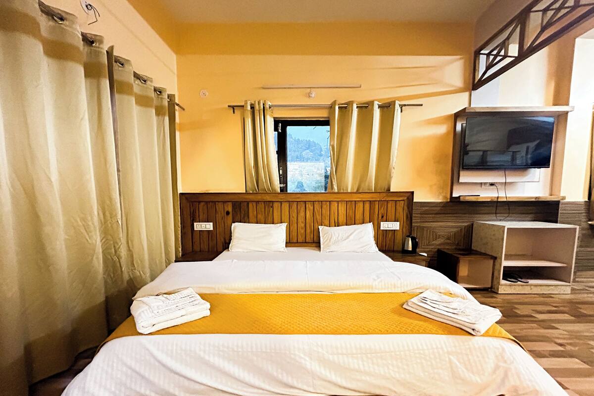 A hotel room with a wooden bed, white bedding, a TV, and a window with curtains.