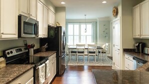 A modern kitchen with white cabinets, stainless steel appliances, and a dining area with white chairs and a table.