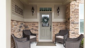 A porch with a stone wall, a door with a wreath, and two wicker chairs.