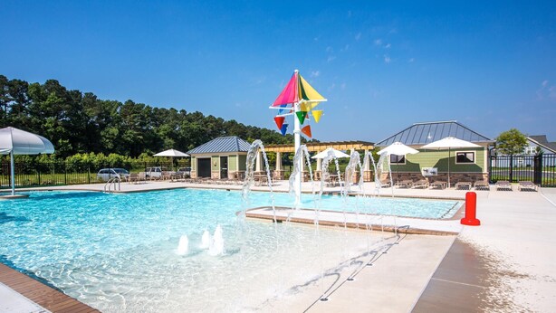 A swimming pool with a water fountain, surrounded by lounge chairs and umbrellas.