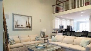A living room with two beige sofas, a coffee table, and a painting of sailboats.