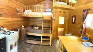 A cozy cabin interior with a bunk bed, a dining table, a stove, and a small kitchen area.