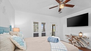 A bedroom with a bed, a ceiling fan, a mounted TV, and a wooden side table with a lantern. - Canalfront | Hot Tub | Boat Slip | Sleeps 10 (Crystal Beach)