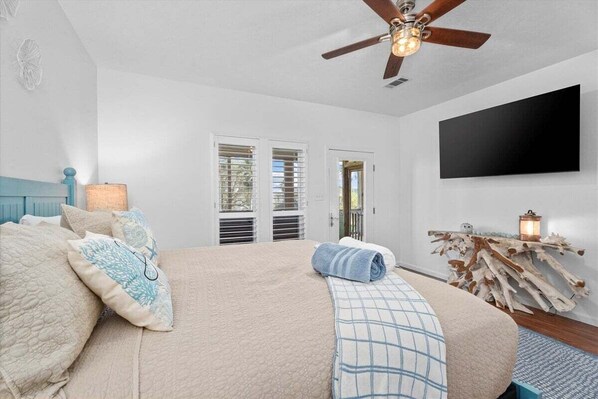 A bedroom with a bed, a ceiling fan, a mounted TV, and a wooden side table with a lantern.
