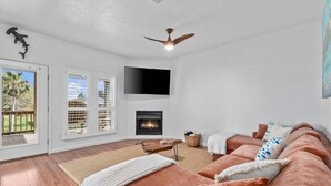 A living room with a fireplace, a television mounted on the wall, and a ceiling fan. - Canalfront | Hot Tub | Boat Slip | Sleeps 10 (Crystal Beach)