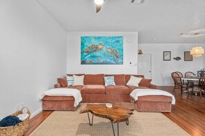 A living room with a brown sectional sofa, a wooden coffee table, and a painting of sea turtles on the wall.