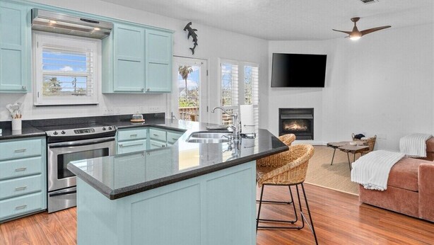 A modern kitchen with light blue cabinets, a central island, and a fireplace. - Canalfront | Hot Tub | Boat Slip | Sleeps 10 (Crystal Beach)