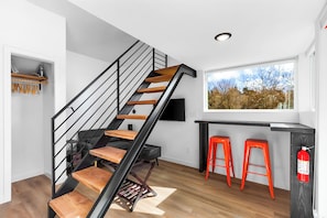 A modern kitchen with a wooden staircase, a black TV, and a window with a view of trees. - Sleek & Stylish Urban Loft (Seattle)