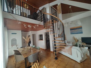 A spacious living area with a wooden staircase leading to an upper level, a dining table with chairs, and a cozy seating area with a sofa and a TV.