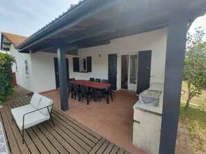 A covered outdoor dining area with a table and chairs, a wooden deck, and a stone feature.