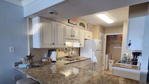 A kitchen with granite countertops, white cabinets, and a refrigerator.