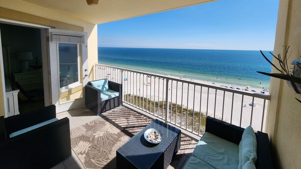 A balcony with a view of the beach, a table with decorative items, and a sofa.
