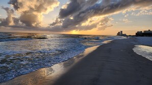 A beach with waves, a sunset, and buildings in the distance.