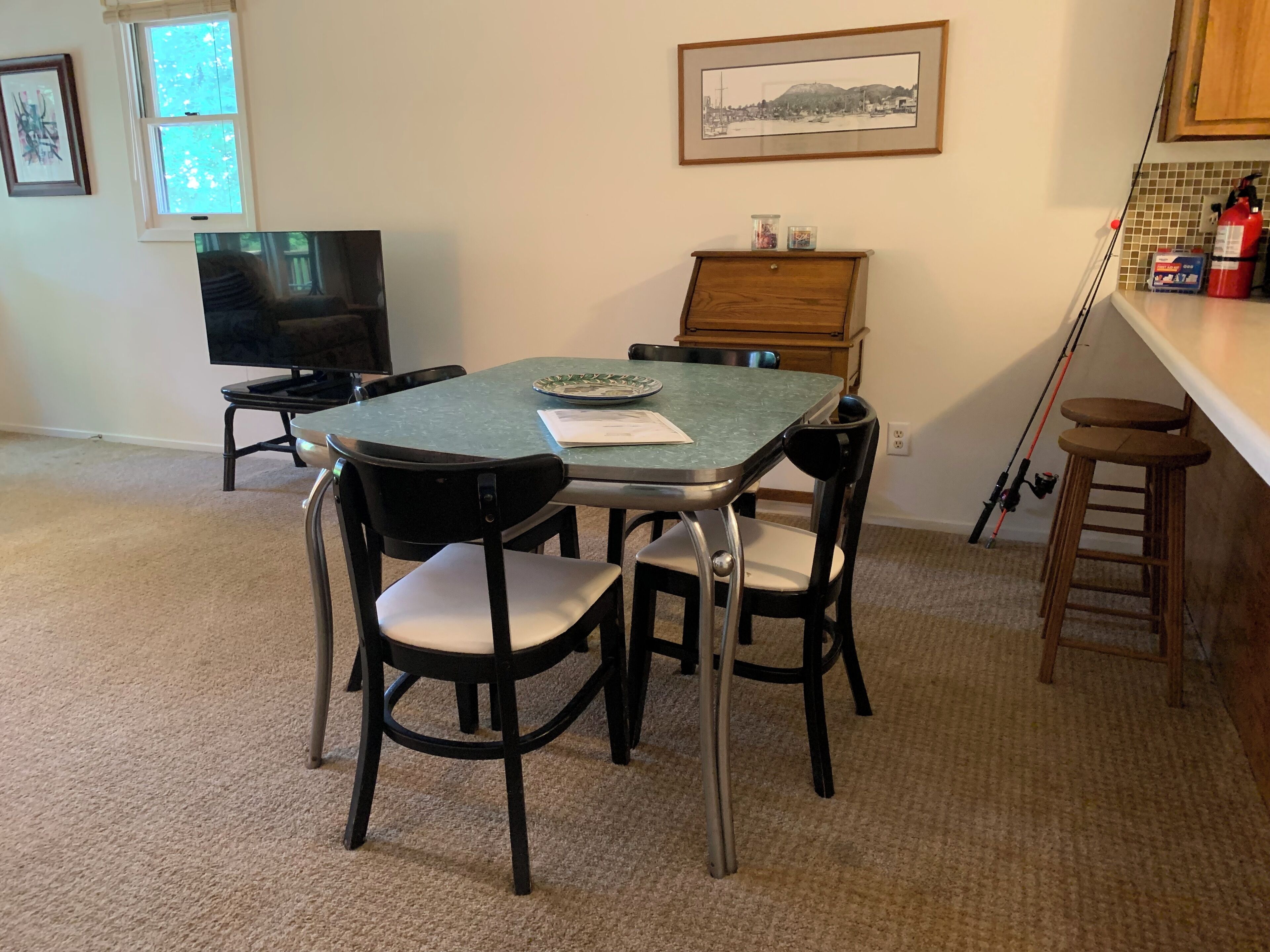 Un comedor con una mesa, sillas, un televisor, un cuadro y una encimera de cocina con una escalera.