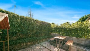 Eine Terrassengruppe im Freien mit einem Holztisch und Bänken, umgeben von einer Steinmauer und üppiger Bepflanzung.