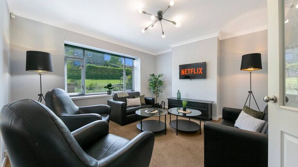 Ein modernes Wohnzimmer mit schwarzen Ledersofas, einem Glastisch und einem an der Wand montierten Fernseher.