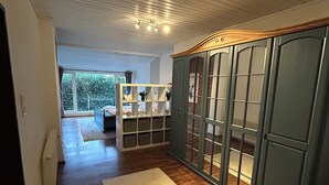 A spacious room with wooden flooring, a large wardrobe with glass doors, and a view of a garden through a window. - Schäferstübchen in Ekern near Bad Zwischenahn (Bad Zwischenahn)