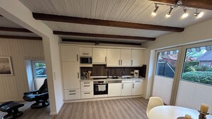 A modern kitchen with white cabinets, a built-in oven, and a dining area with a table and chairs. - Schäferstübchen in Ekern near Bad Zwischenahn (Bad Zwischenahn)