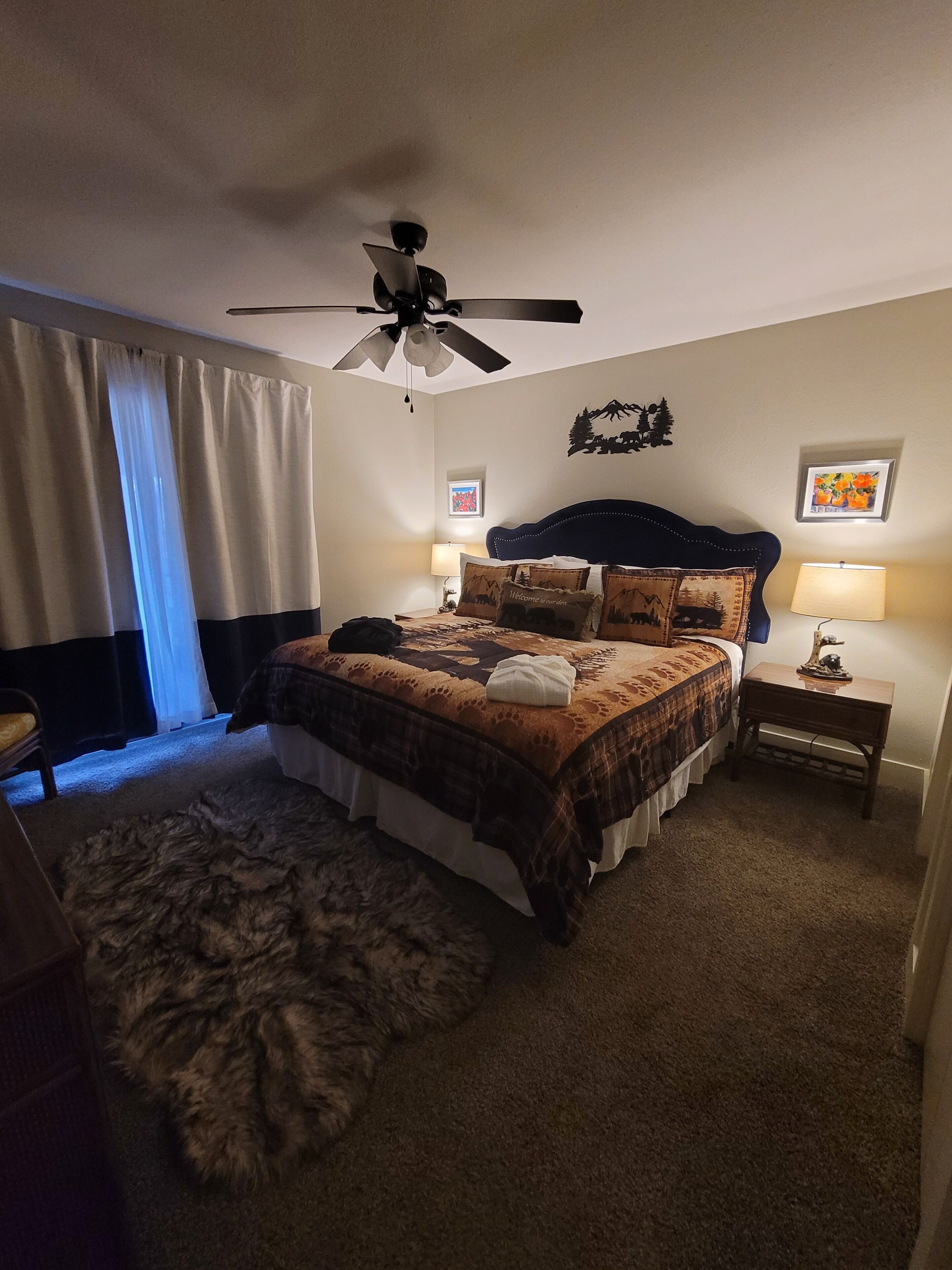 Een slaapkamer met een bed, een plafondventilator, een tapijt en twee nachtkastjes met lampen.