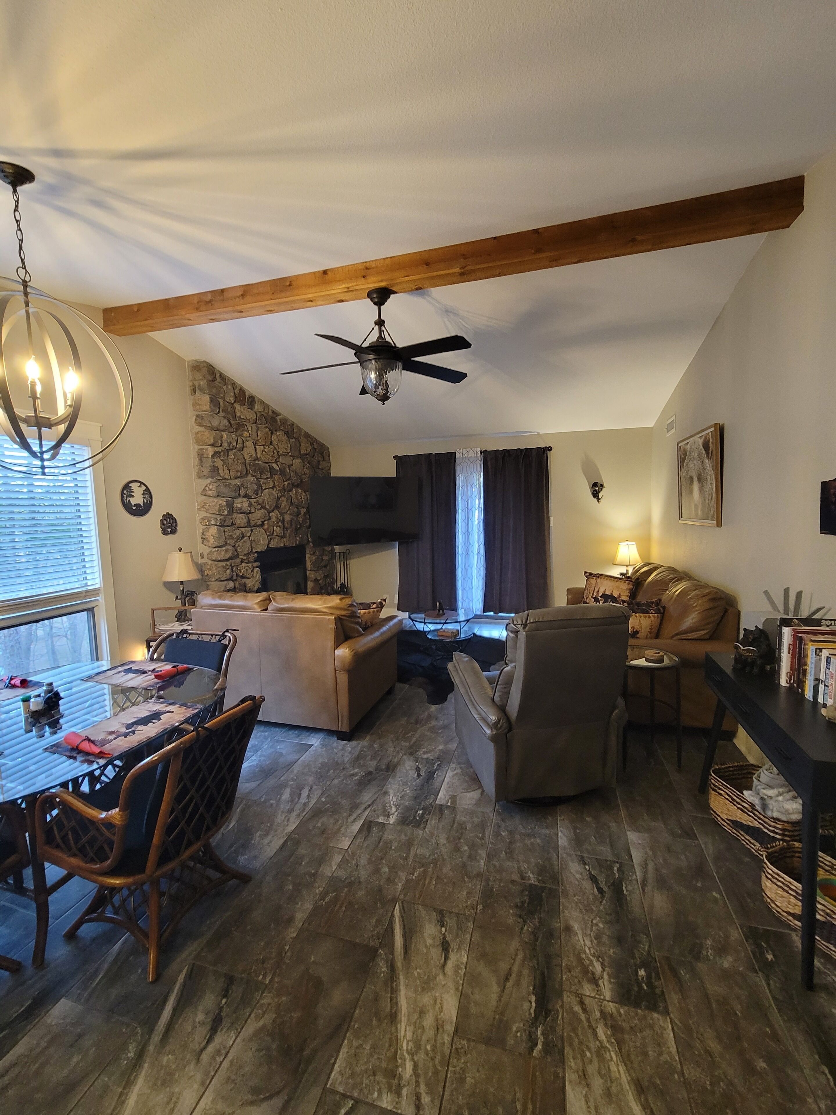 Una sala de estar acogedora con pared de piedra, chimenea, ventilador de techo y comedor con mesa y sillas.