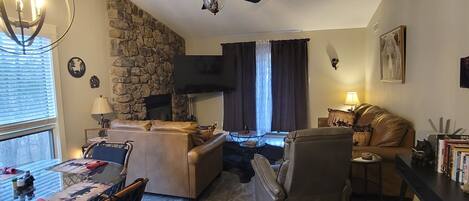 Una sala de estar acogedora con pared de piedra, chimenea, ventilador de techo y comedor con mesa y sillas.
