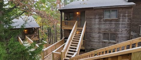 A wooden cabin with a wooden deck and stairs leading to the main building.