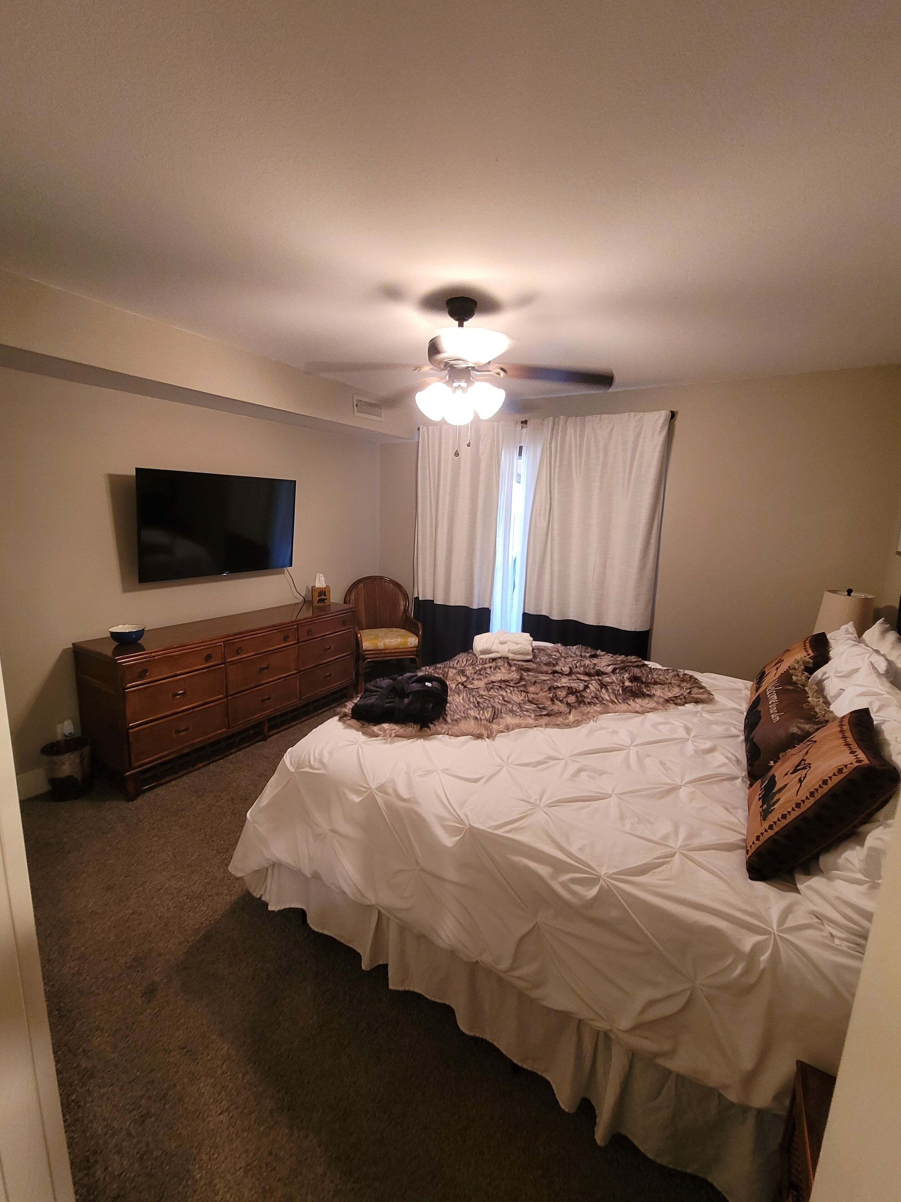 A bedroom with a bed, a dresser, a television, and a ceiling fan.
