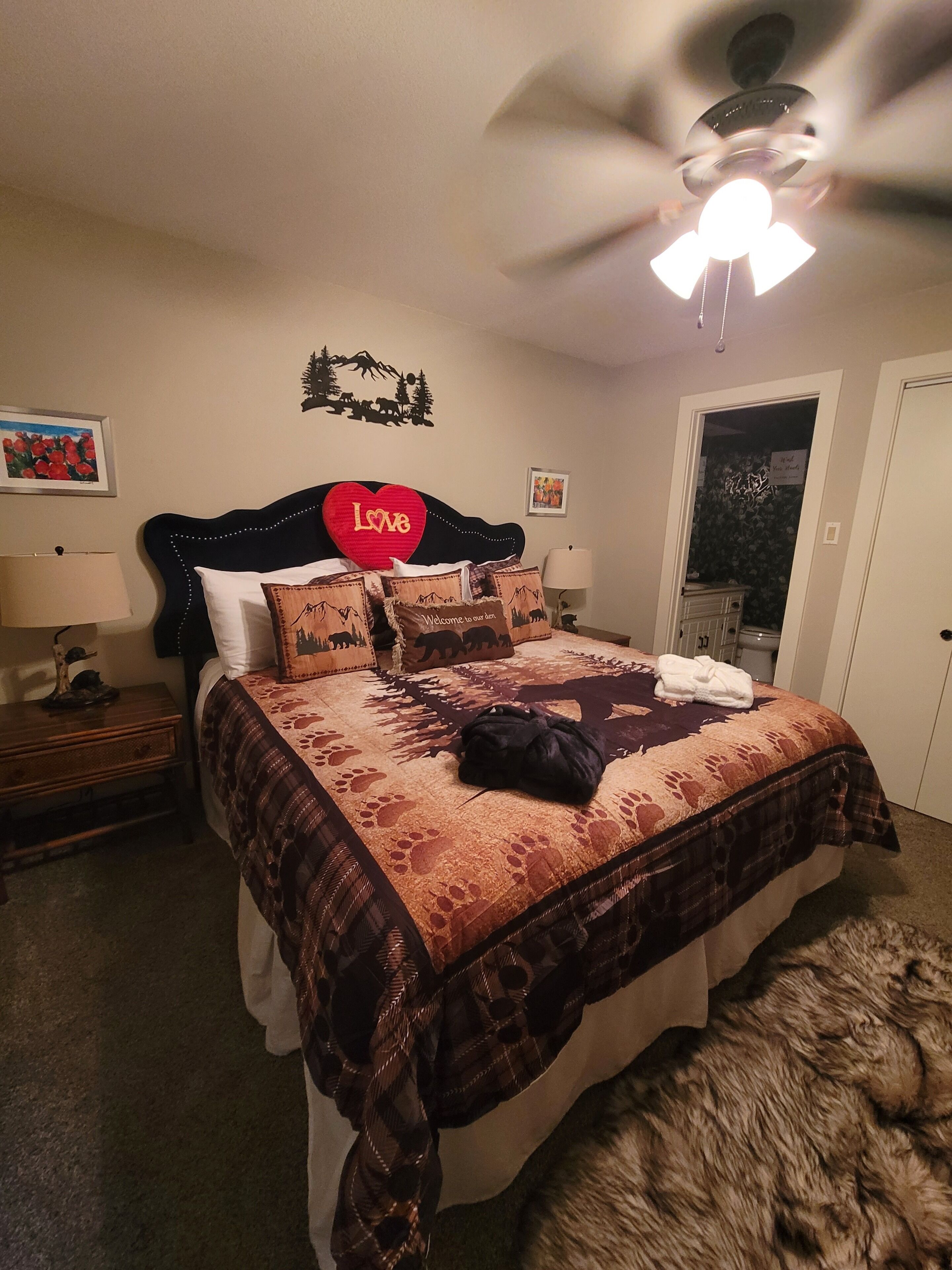 Une chambre à coucher avec un lit, un ventilateur de plafond, une table de chevet et un tapis moelleux.