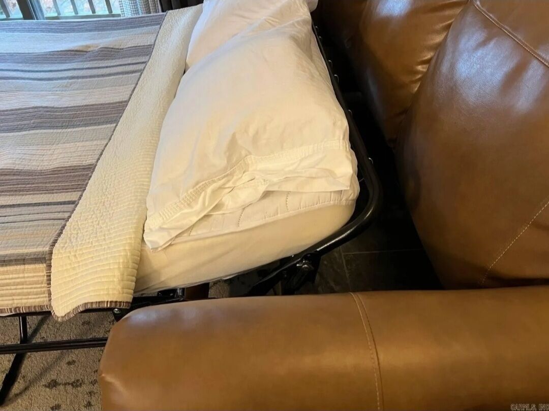 Una silla de cuero marrón con un cojín blanco y una manta a rayas.